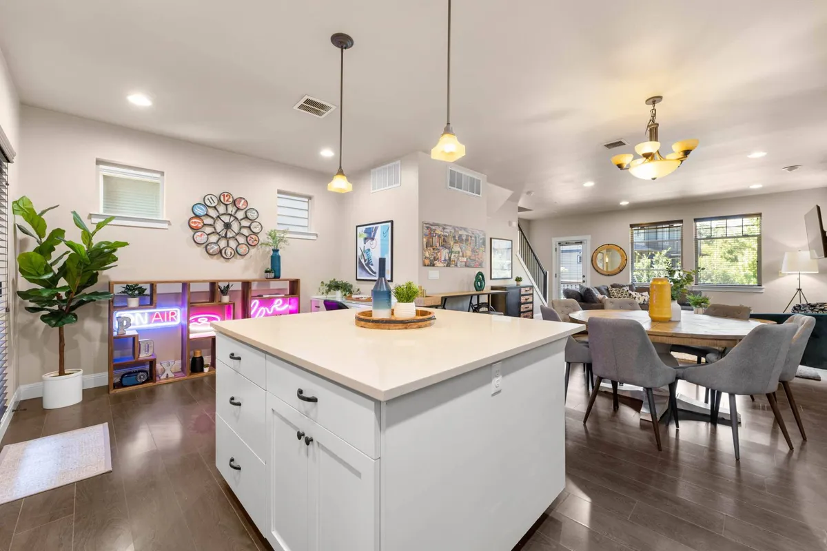 A vibrant kitchen space with a central island, colorful wall clock, comfortable seating area, and playful art pieces. The atmosphere is energetic and inviting, ideal for both meal prep and socializing.