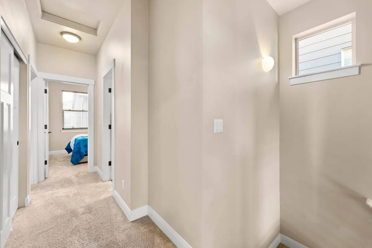 A bright hallway filled with natural light, featuring open doorways and a glimpse of the home's communal spaces. The scene suggests activity, movement, and the potential for guests to come and go throughout the day.