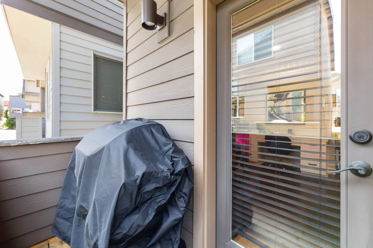 An exterior shot highlighting a covered BBQ grill, the adjacent door with blinds, and textured exterior walls. The setup is casual and comfortable, suggesting outdoor dining and gatherings in a relaxed environment.