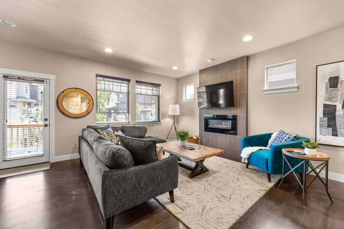 The image showcases a spacious, stylish living room with a plush sofa, modern coffee table, striking fireplace, curated artwork, and a decorative mirror. The space exudes warmth and creativity, inviting guests to relax, entertain, or gather for cozy evenings.
