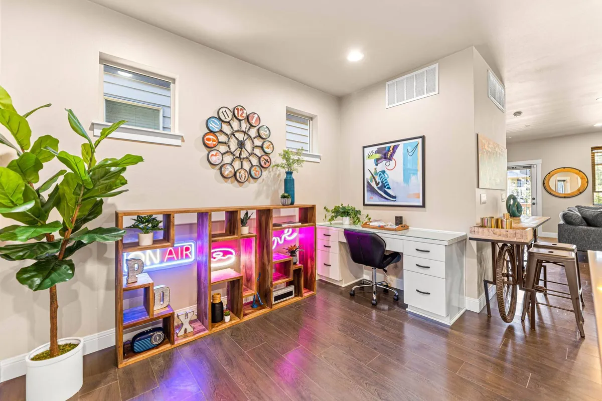 A creatively styled interior space with a decorative wall clock, neon sign, eye-catching artwork, a green plant, and a desk and chair setup. The decor exudes a boutique, art-focused ambiance, with vibrant colors and curated pieces.