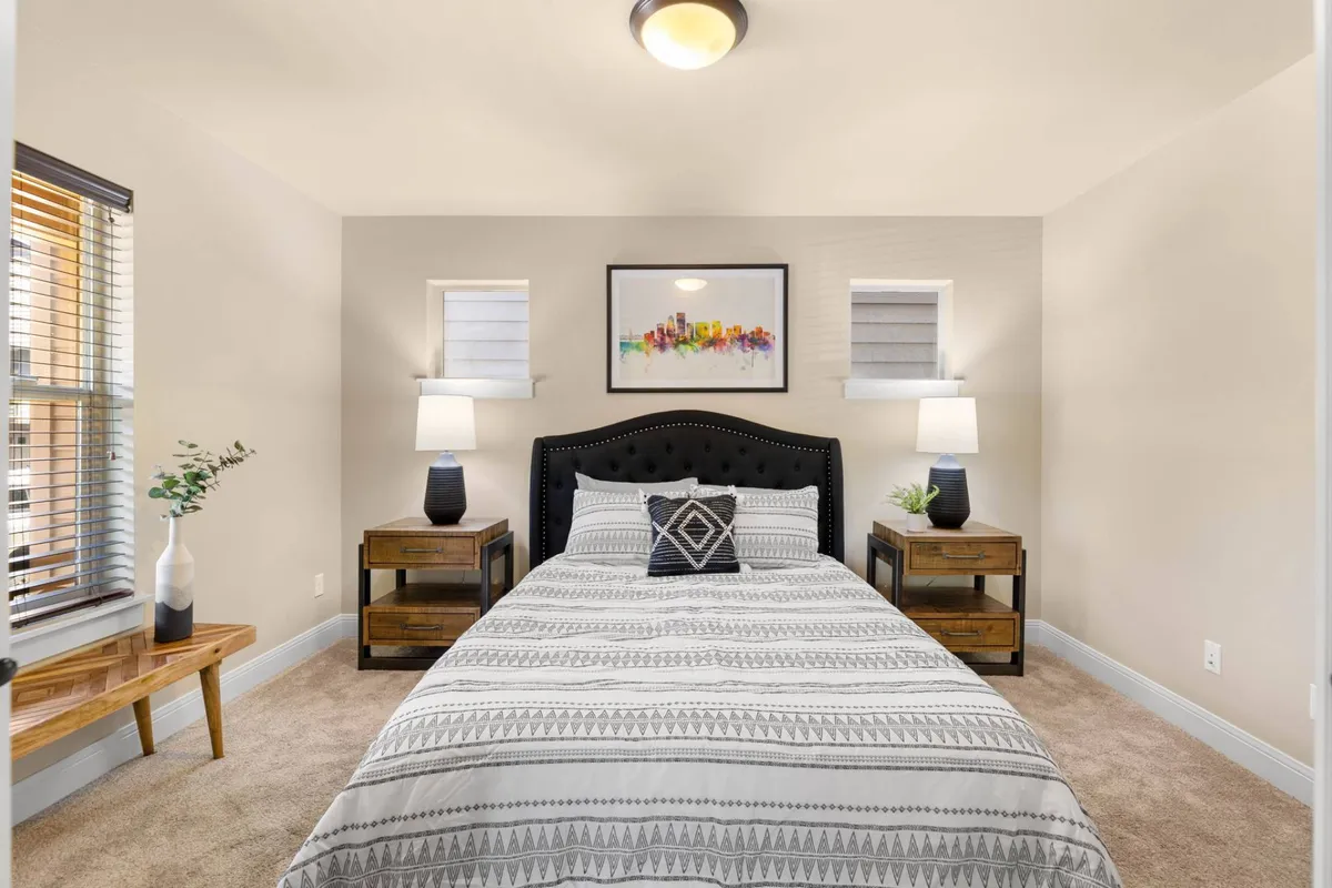 A tranquil bedroom scene featuring a well-made bed with plush linens, nightstands on either side adorned with lamps, and tasteful artwork above the headboard. The soft color palette and gentle lighting create a peaceful, restorative atmosphere ideal for relaxation.
